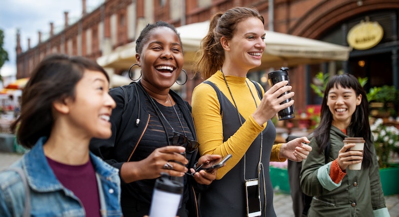 A group of friends walk  through a city street holding coffee cups. 