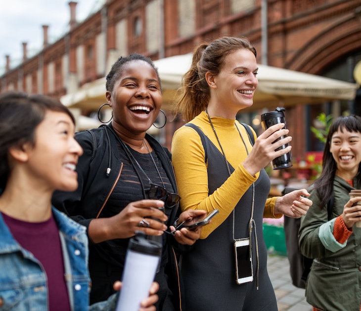 A group of friends walk  through a city street holding coffee cups. 